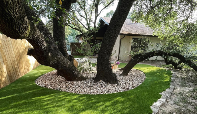 Residential backyard with mature trees surrounded by installed artificial turf 